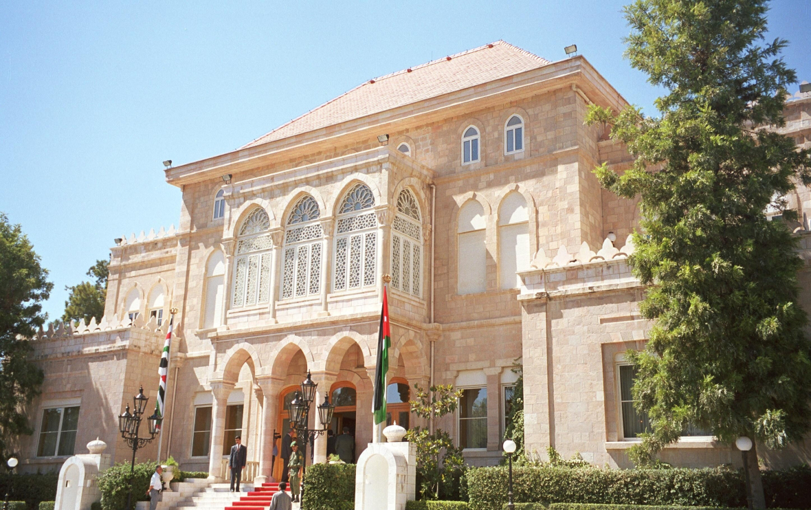 Ein Palast gebaut aus hellem Stein. An einem Fahnenmast hängt die jordanische Flagge. 