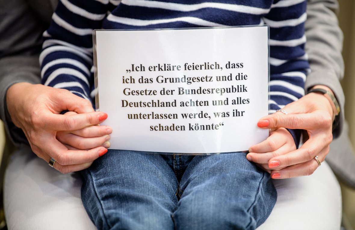 Ein kleiner Junge zeigt einen Zettel mit dem Eid auf die Verfassung. Bei der Einbürgerungsfeier in Bayern sprechen die neuen Staatsbürgerinnen und Staatsbürger diesen Text.