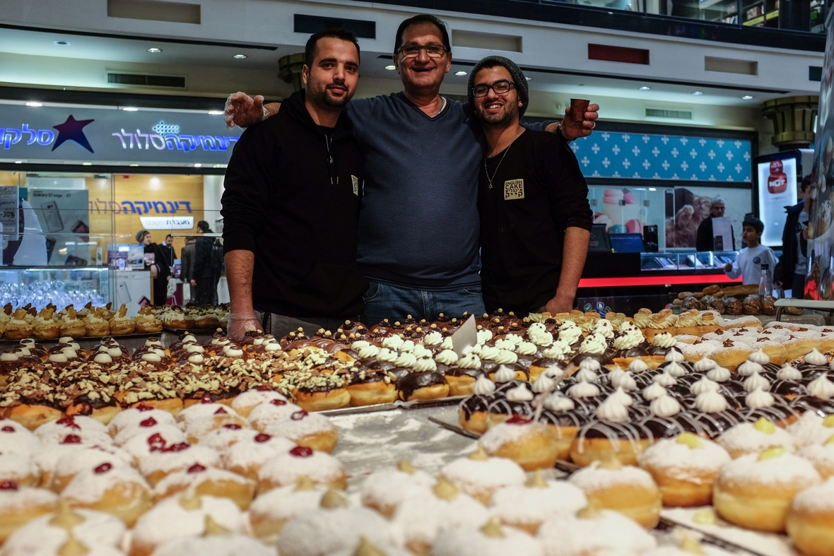 Traditionelles Chanukka Gebäck in einer Bäckerei in Jesursalem, Israel. Der Vater präsentiert stolz das Gebäck gemeinsam mit seinen beiden Söhnen.