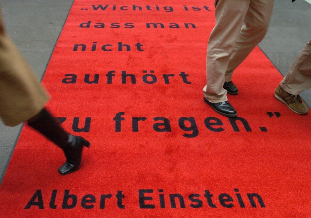 "Wichtig ist, dass man nicht aufhört zu fragen". Zitat von Albert Einstein auf einem Teppich zum Einstein-Jahr 2014. Über diesem Teppich laufen in Berlin mehrere Menschen.