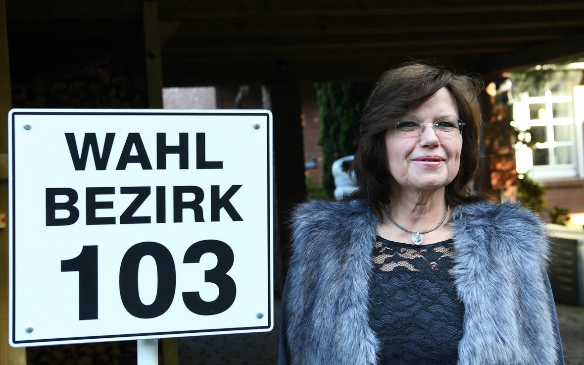 Ein Schild mit der Aufschrift "Wahlbezirk 103", neben dem eine Frau steht, weist darauf hin, wo die Wahlberechtigten dieses Wahlbezirks in Niedersachsen ihre Stimme abgeben können. 
