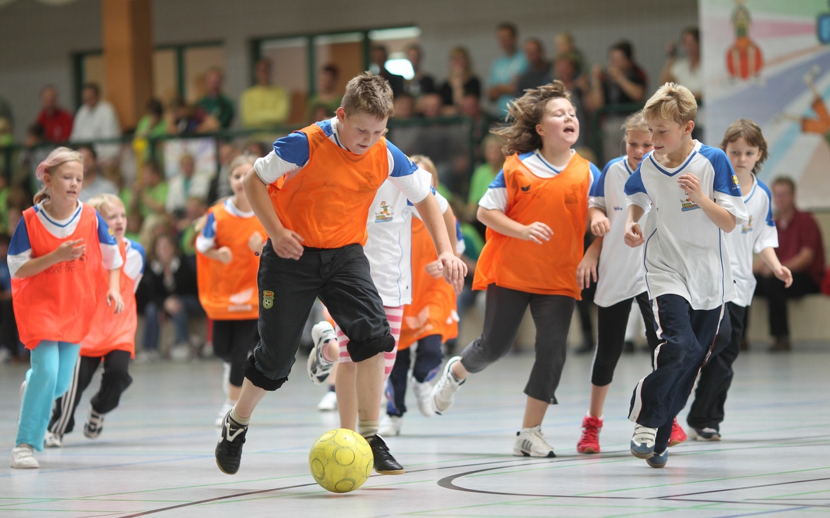 Schulkinder kicken in einer Sporthalle miteinander