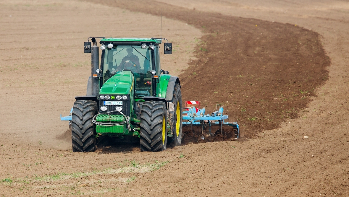 Ein Landwirt sitzt auf einem Traktor, mit dem er ein Feld bearbeitet. 