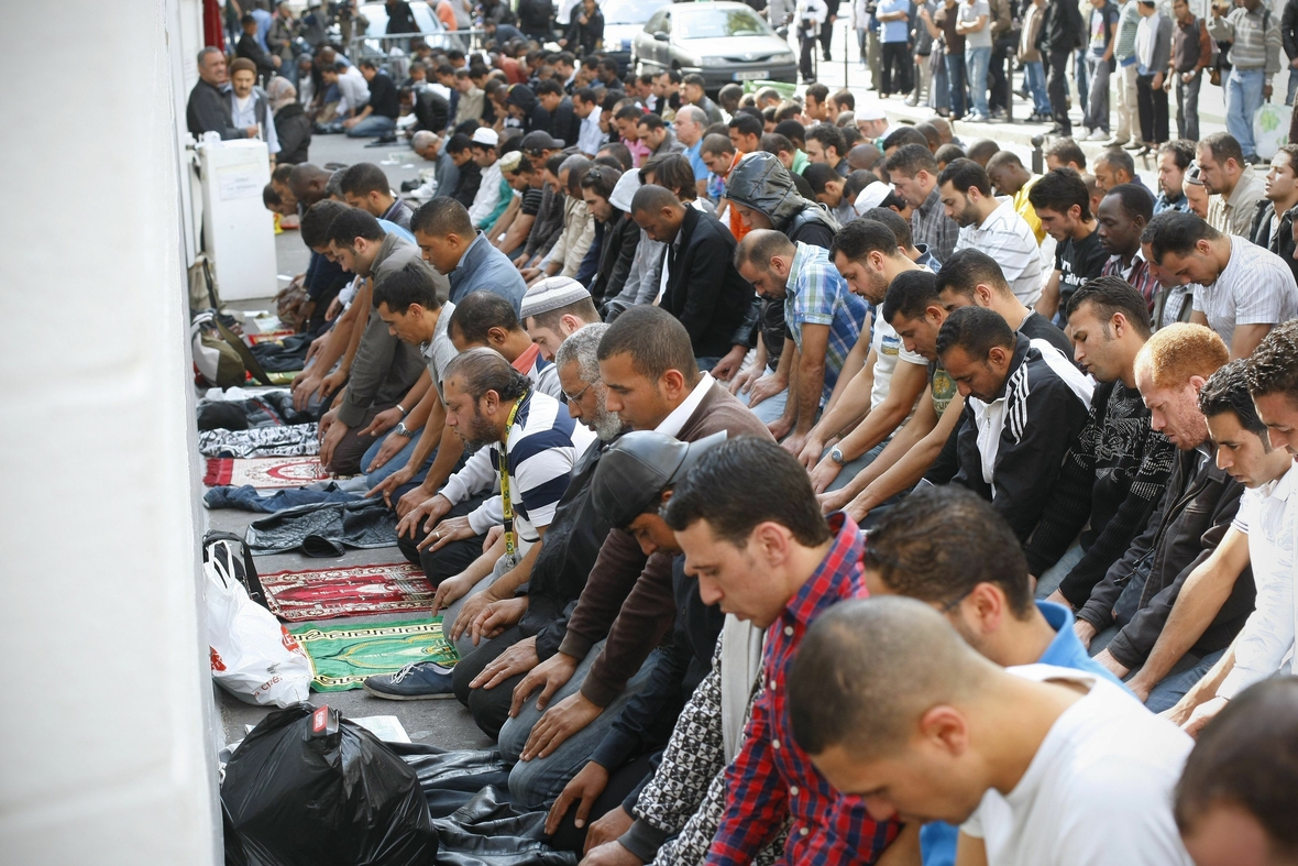 Betende Muslime auf einer Straße in Paris. Viele Männer sitzen in Gebetshaltung nebeneinander.