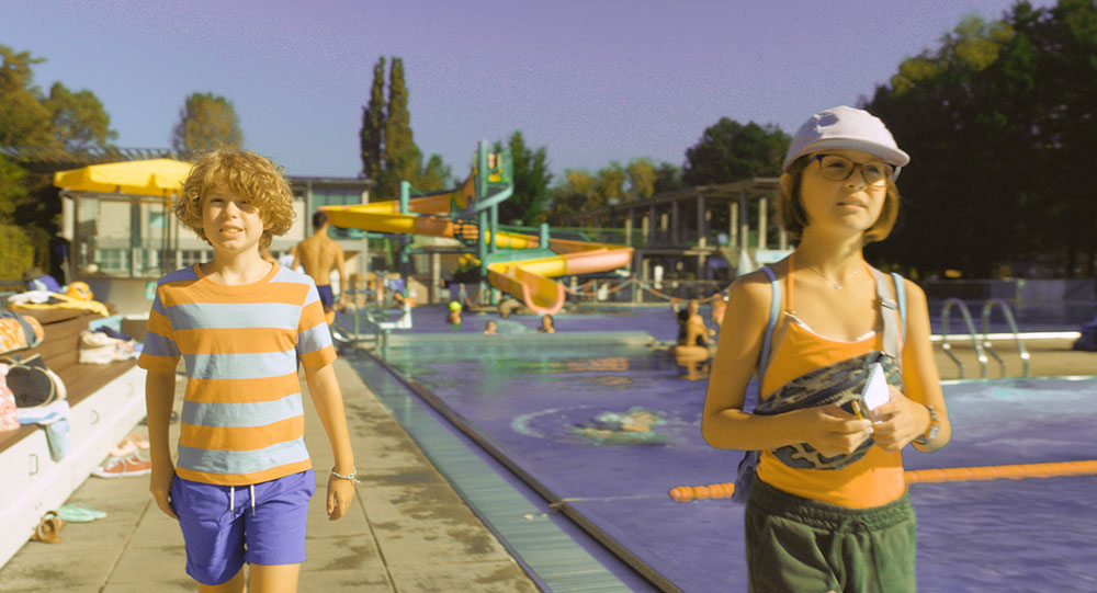 Szenenbild: Franz (links im Bild) und Gabi (rechts im Bild) im Schwimmbad. Rechts hinter Gabi sieht man das Schwimmbecken.