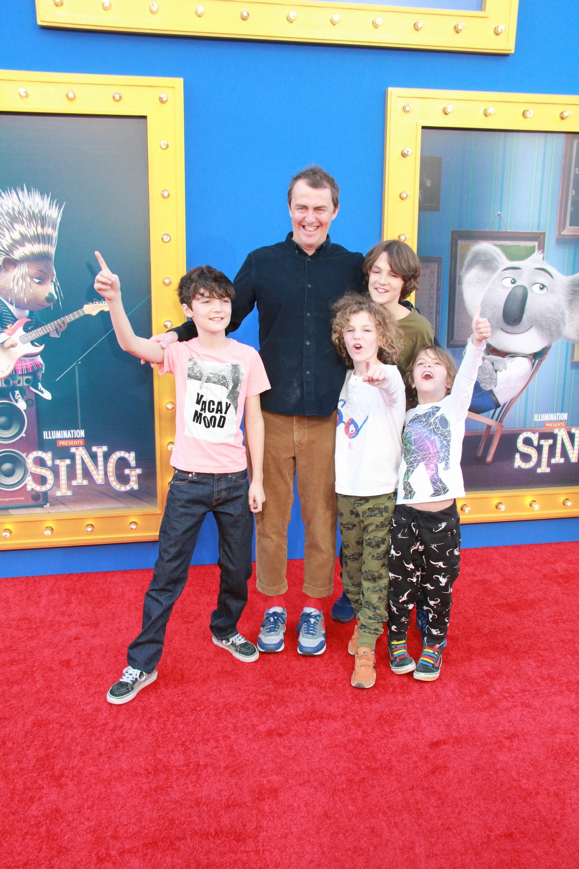Der Regisseur Garth Jennings umringt von vier begeisterten Kindern bei der Weltpremiere des Films in den USA. Im Hintergrund sind Plakate des Films zu sehen.