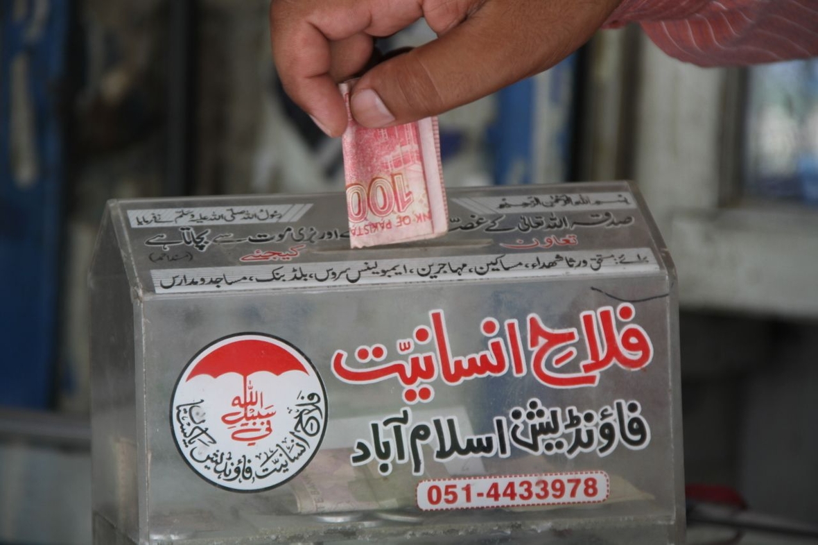 Eine Hand steckt Geld in eine Sammelbox, mit der während des Ramadan in Pakistan Spenden gesammelt werden.