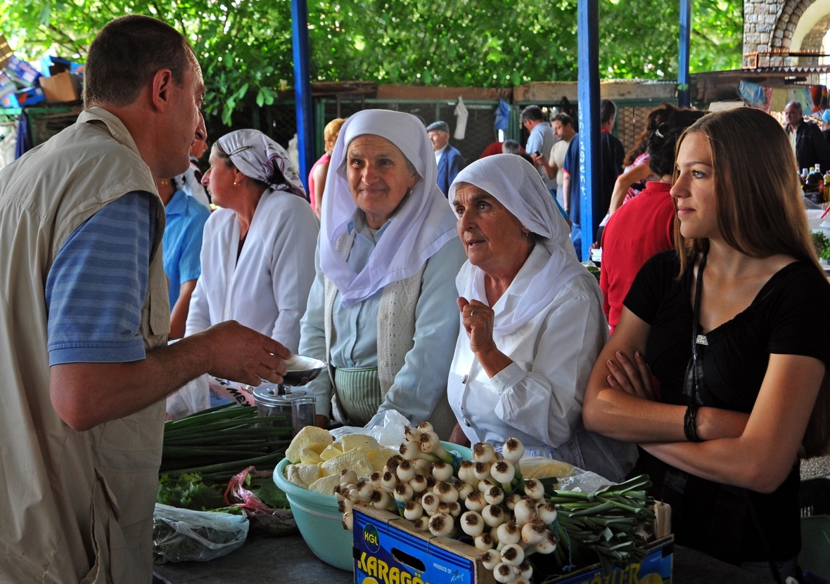 Frauen im Gespräch mit einem Gemüsehändler auf dem Markt der Stadt Ulcinj. Die Stadt gehört zu den beliebtesten Reisezielen in Montenegro.