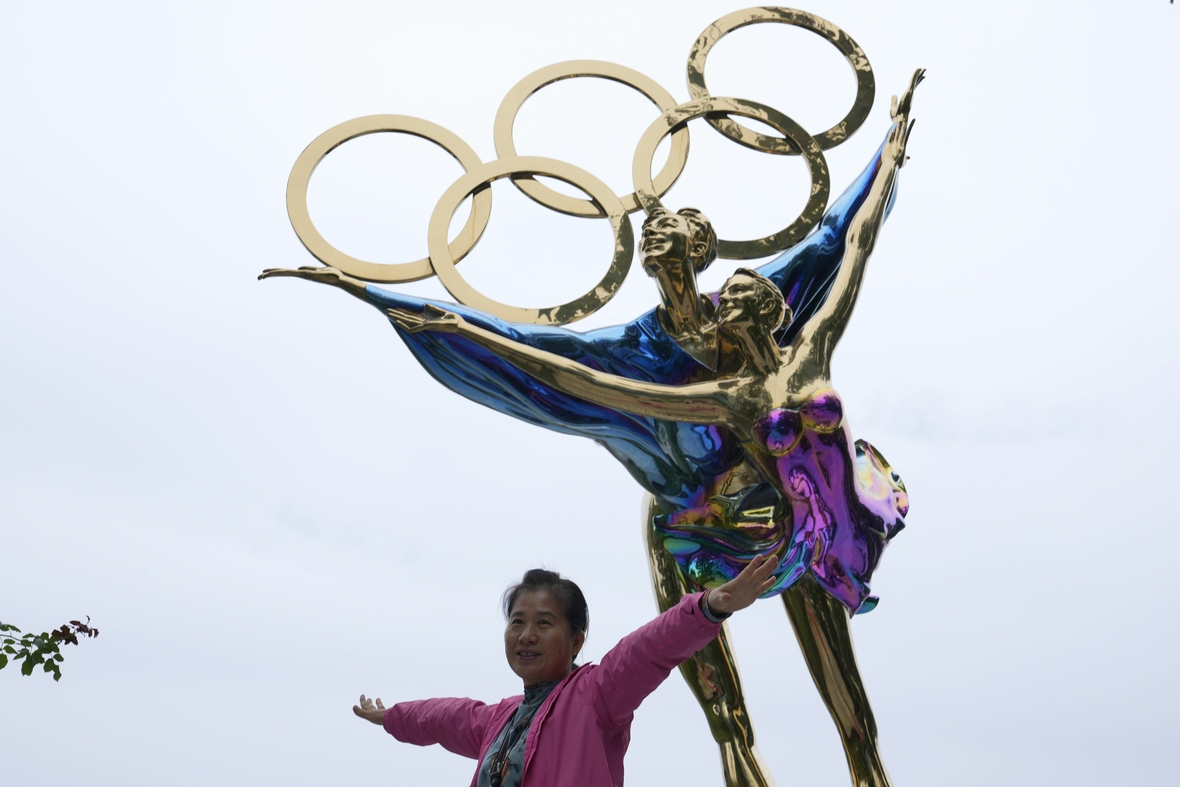 Spaziergängerin vor einer Statue im Shougang Park in Peking. Die Statue besteht aus einem Eiskunstläufer-Paar und den Olympischen Ringen und ist ein Symbol für die Olympischen Winterspiele 2022, die in Peking stattfinden.