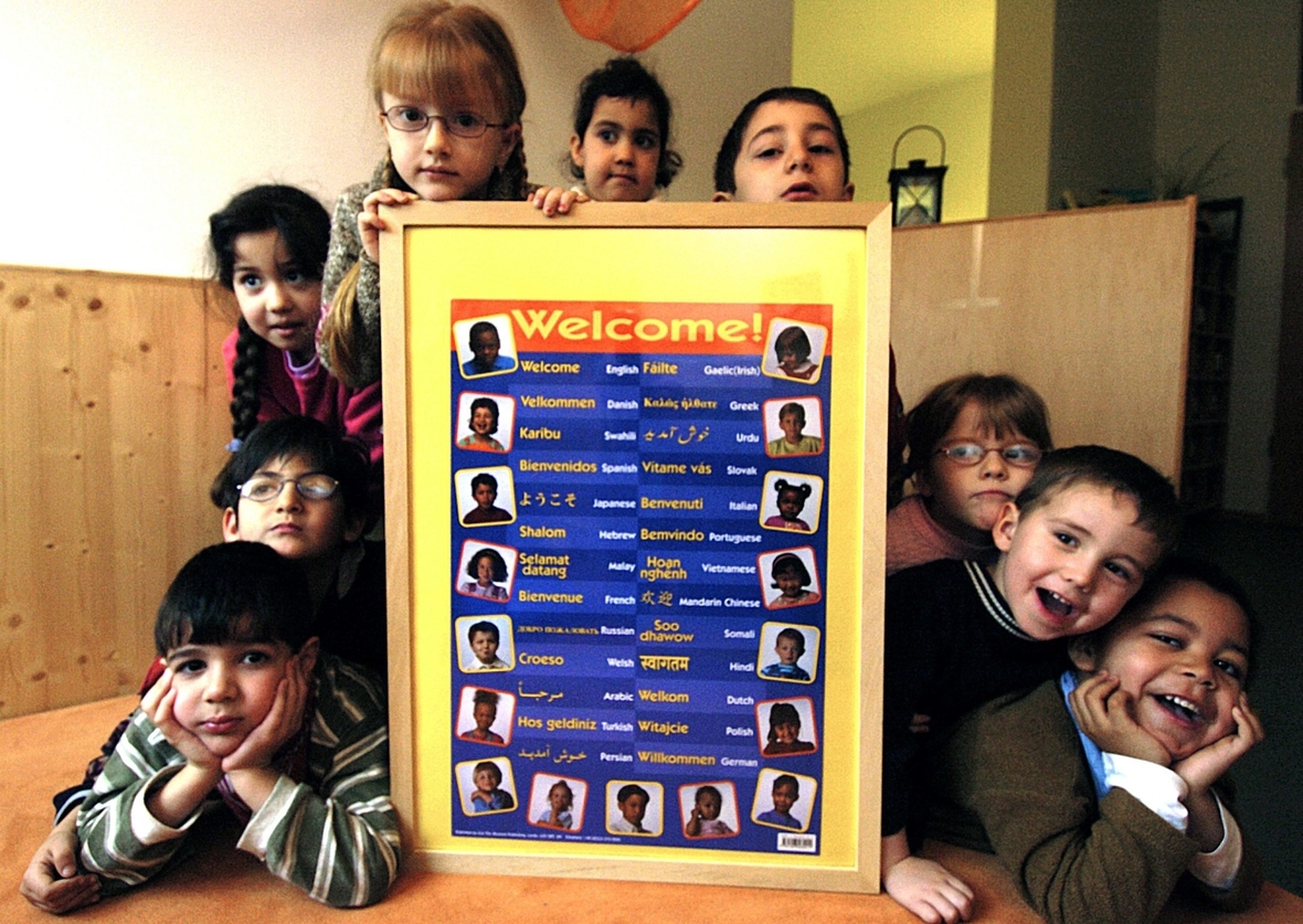Frühstarter: Kindergartenkinder zeigen ein Schild, auf dem sie "Willkommen" in viele andere Sprachen übersetzt haben.