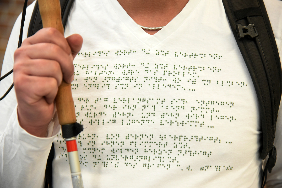 Ein blinder Student trägt ein T-Shirt, auf dem in Blindenschrift ein Gedicht eingestickt ist.