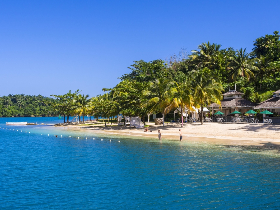 Man sieht Strand und Meer in der Sonne. Ein karibischer Strand mit Badegästen, Jamaika.