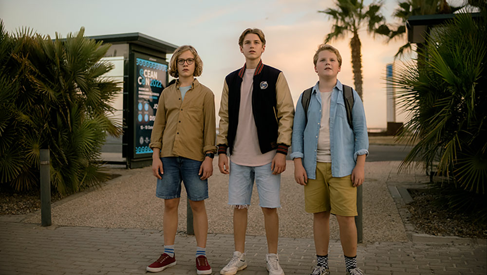 Szenenbild: Von links nach rechts: Bob, Peter und Justus am Strand von Rocky Beach mit Palmen.