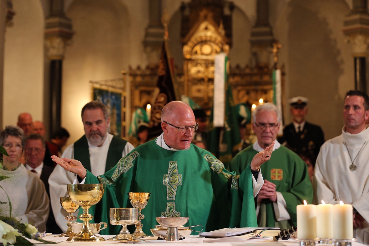 Der katholische Priester feiert die Eucharistie (das Abendmahl). Er steht am Altar, hebt die Hände zum Gebet. Auf dem Altar steht ein Hostienteller.