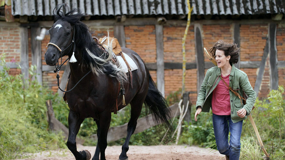 Szenenbild: Ari (rechts im Bild) läuft neben Ostwind (links im Bild) her. Sie versucht so, das Pferd auf das Kunstreiten vorzubereiten.