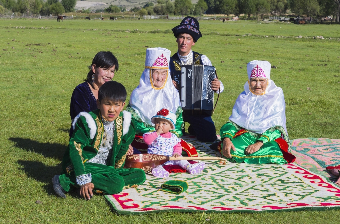 Kasachische Familie in traditioneller Kleidung hört der Musik eines Akkordeonspielers im Tian Shan Hochgebirge zu.