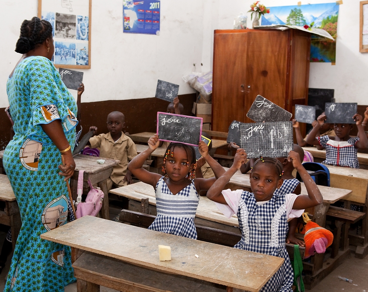 Eine Schule in der Hafenstadt Grand-Bassam, Elfenbeinküste. Die Schüler und Schülerinnen notieren ihr Ergebins der Aufgabe auf einer kleinen Tafel und halten die Tafel hoch.
