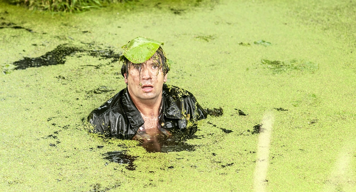 Szenenbild: Lehrer Franz schwimmt in einem Teich und hat ein Blatt auf dem Kopf
