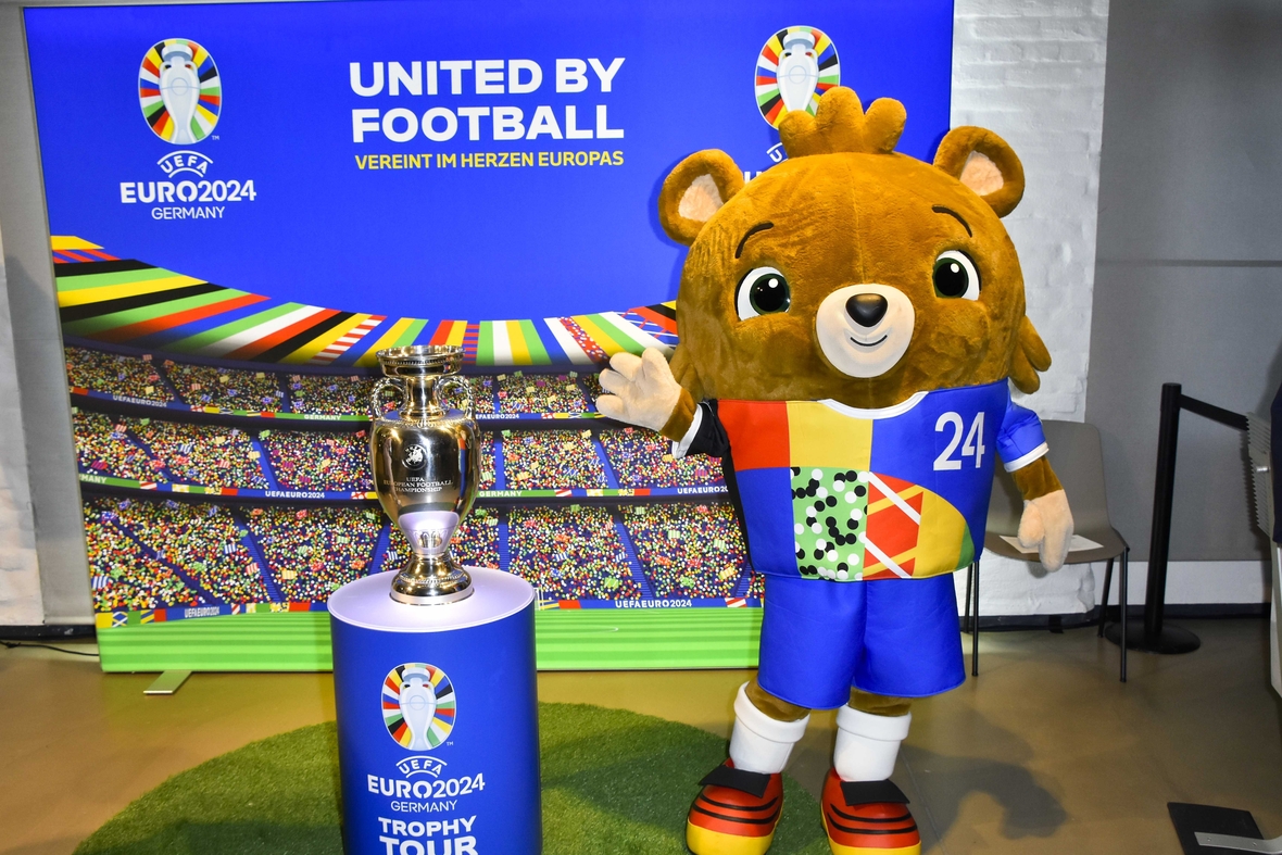 Das offizielle Maskottchen der UEFA EURO 2024 heißt Albärt und ist ein Teddybär (rechts). Links daneben steht der Original Henri-Delaunay-Pokal, der seit 1960 als Trophäe dem Gewinner der Fußball-Europameisterschaft verliehen wird.