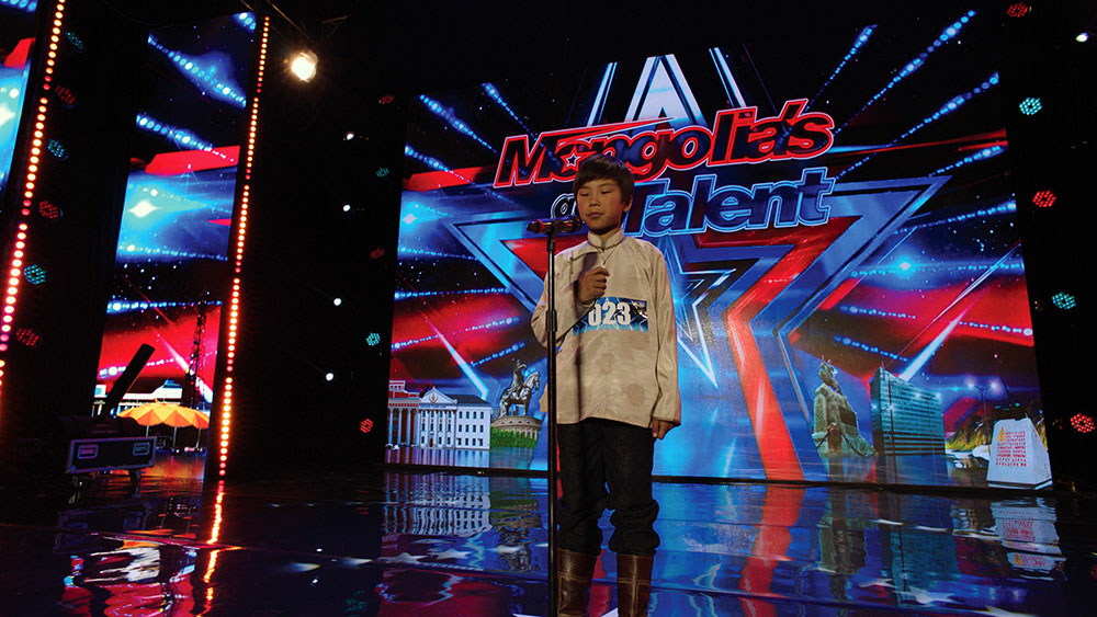 Der Junge Amra steht auf einer Bühne. Er singt in der großen Talentshow des Fernsehens.