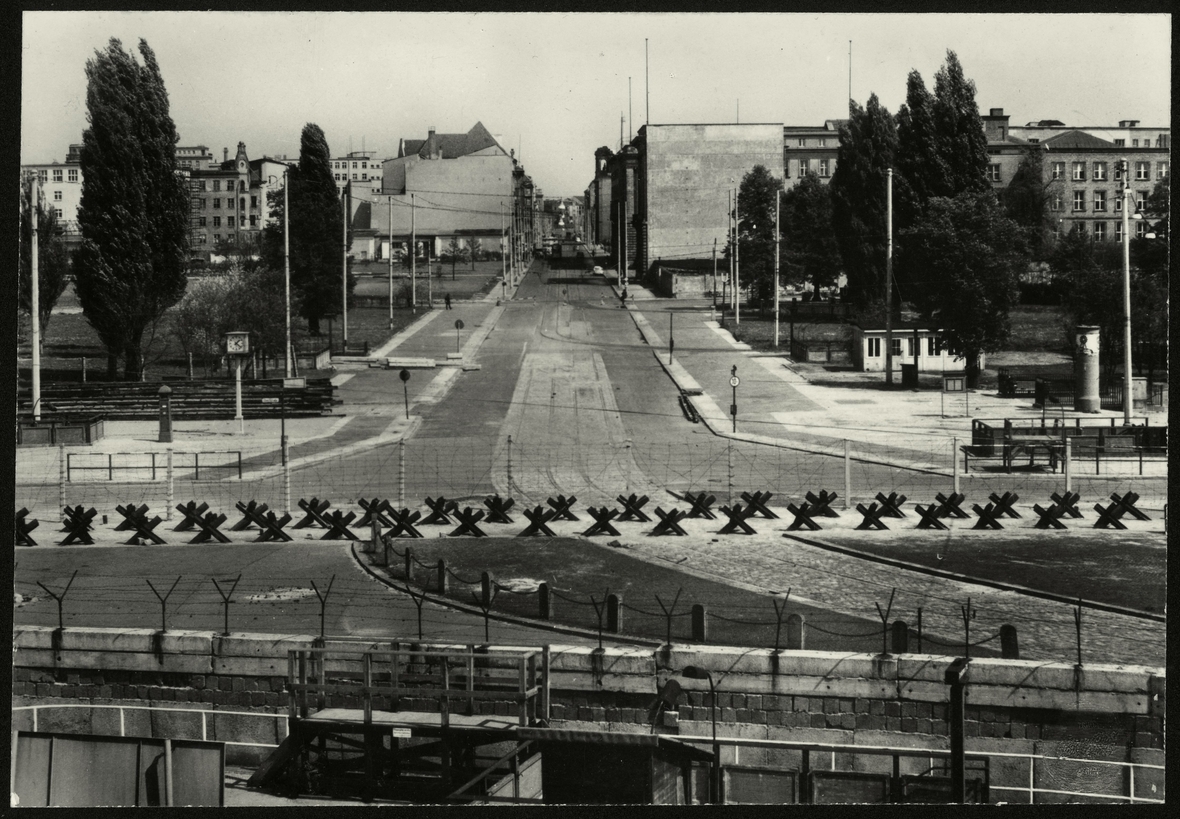 Die Foto-Postkarte von um 1963 zeigt im Vordergrund die Berliner Mauer. Zu sehen sind dahinter Panzersperren am Potsdamer Platz sowie ein Blick auf den Leipziger Platz und in die Leipziger Straße.