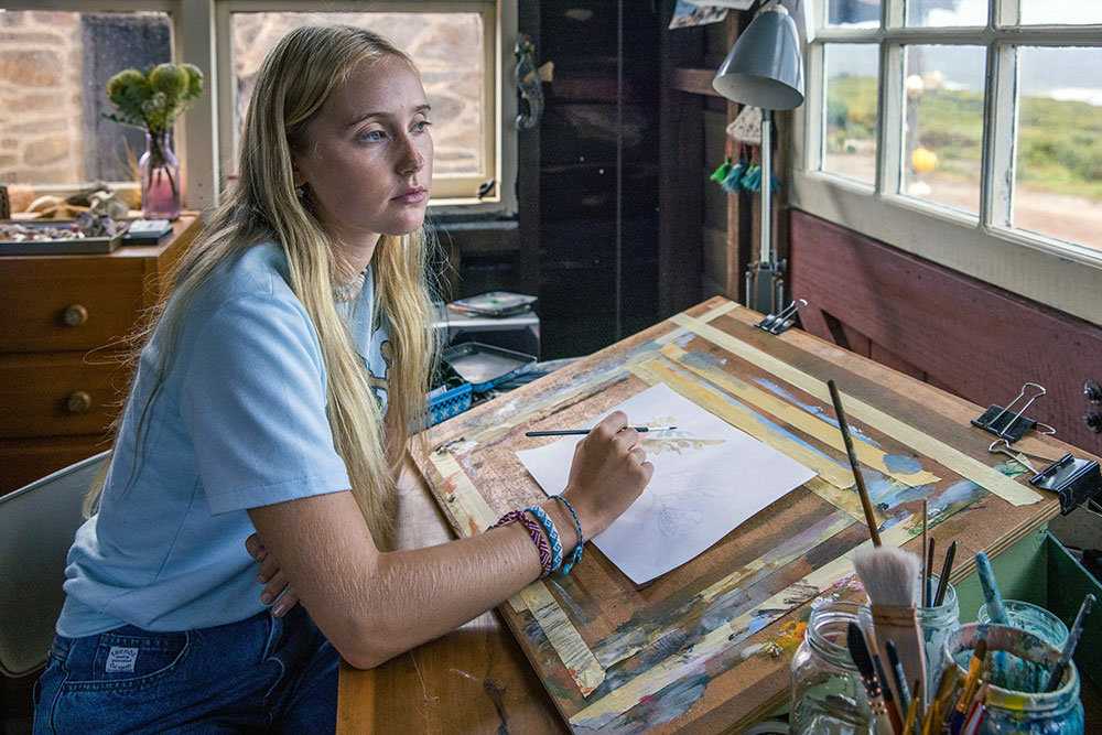 Szenenbild: Abby als Teenager (links im Bild) sitzt an ihrem Schreibtisch und bildet die Unterwasserwelt in ihren Zeichnungen ab.