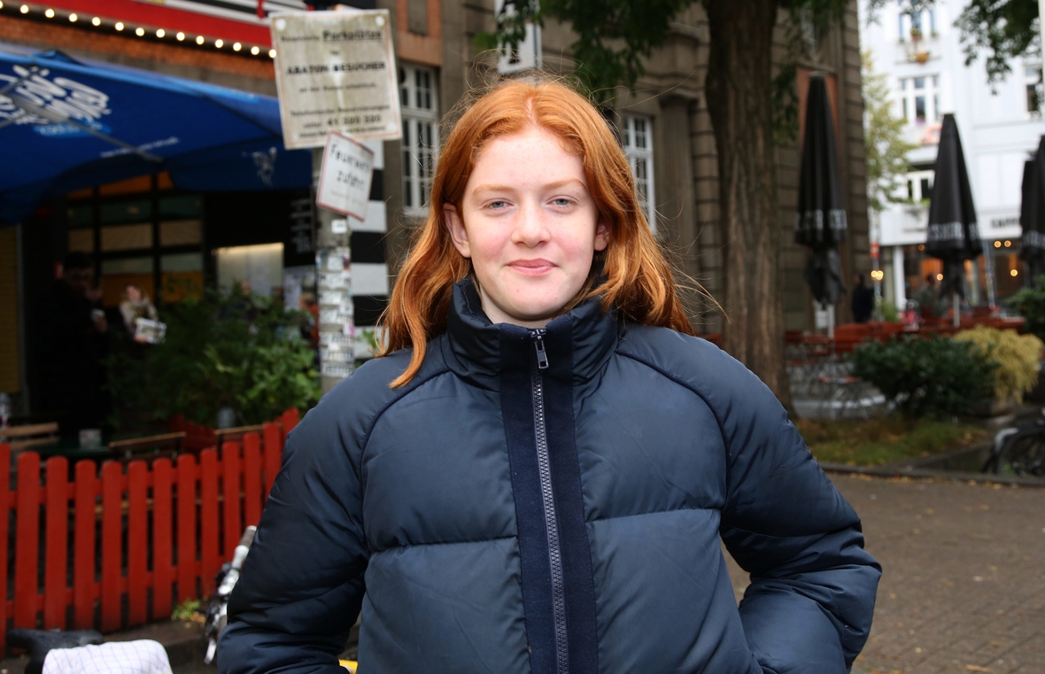 Gerda Lie Kass mit roten Haaren und einer blauen Steppjacke lächelt in die Kamera. Sie ist die Hauptdarstellerin des Films Wildhexe.