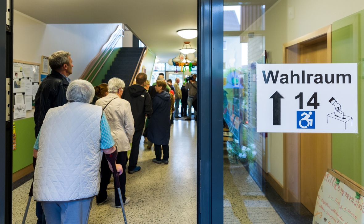 Wählerinnen und Wähler stehen in Schwerin (Mecklenburg-Vorpommern) vor einem Wahllokal in einer Schlange an.