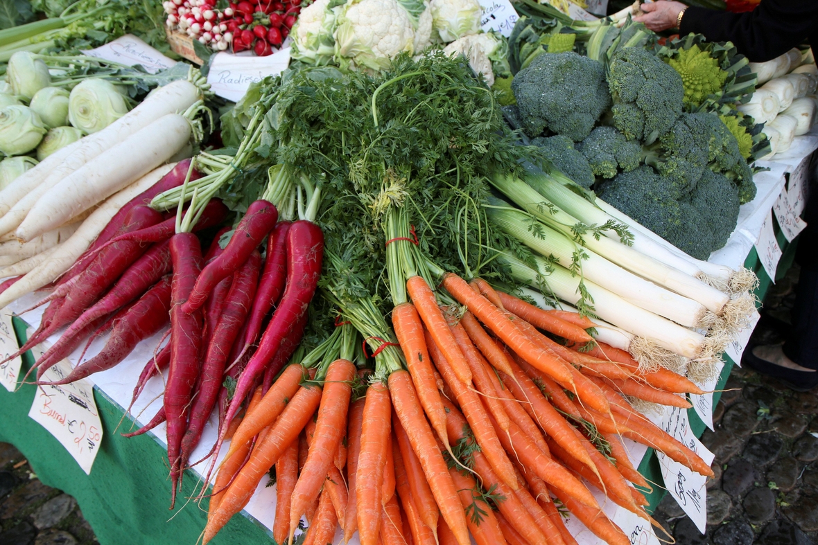 Auf einem Wochenmarkt gibt es eine große Auswahl an Gemüsesorten. Hier liegt ein Bund Möhren neben Rettich, Brokkoli und Zwiebelchen.