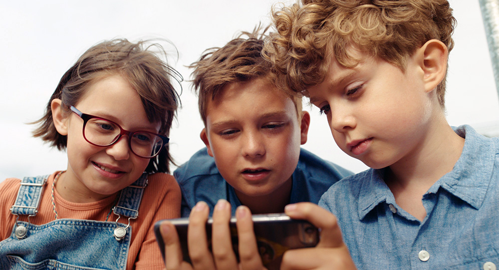 Szenebild: Gabi, Eberhard und Franz (von links nach rechts) stehen eng zusammen und sehen ein Video auf dem Smartphone.