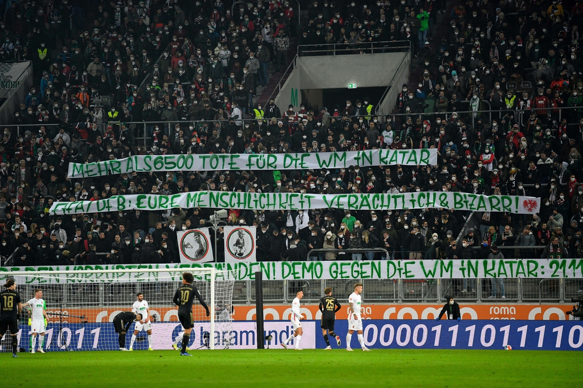 Beim Spiel des FC Augsburg gegen den FC Bayern München im November 2021 zeigen Zuschauer Plakate gegen die Ausbeutung in Katar im Zusammenhang mit der Fußball-WM und rufen zur Demo auf.