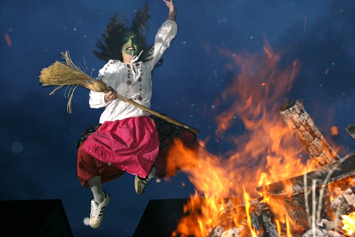 Ein als Hexe verkleideter Mensch springt über ein Feuer während der Feier der Walpurgisnacht im Harz.