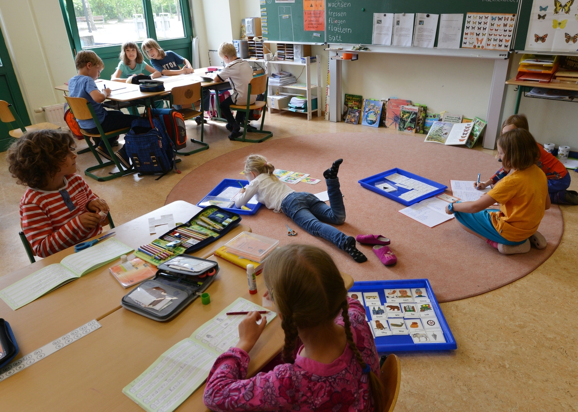 Altersgemischte Lerngruppe in einer Montessori-Grundschule. Die Kinder arbeiten, dabei sitzen an Tischen, hocken oder liegen auf dem Boden