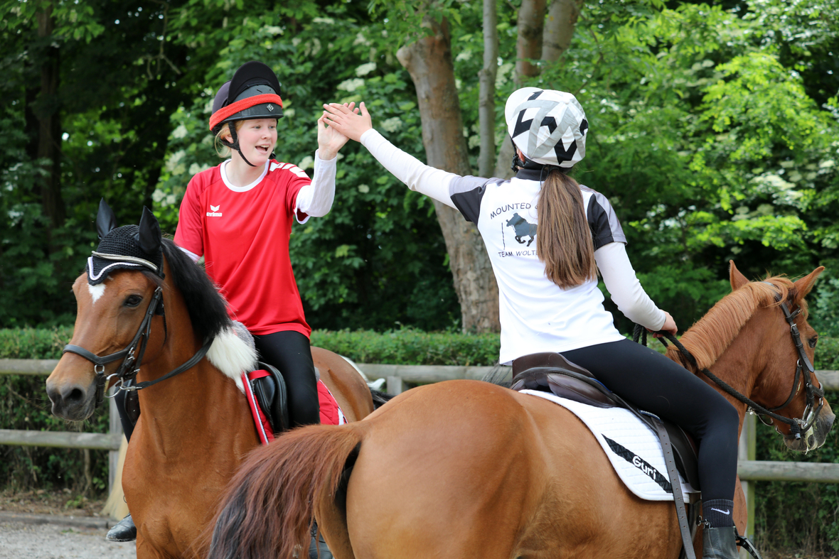 Zwei Mädchen klatschen sich beim Reiten auf ihren Ponies ab. Das Abklatschen nach einem Wettkampf gilt als Zeichen des respektvollen Miteinanders und fairen Spiels.