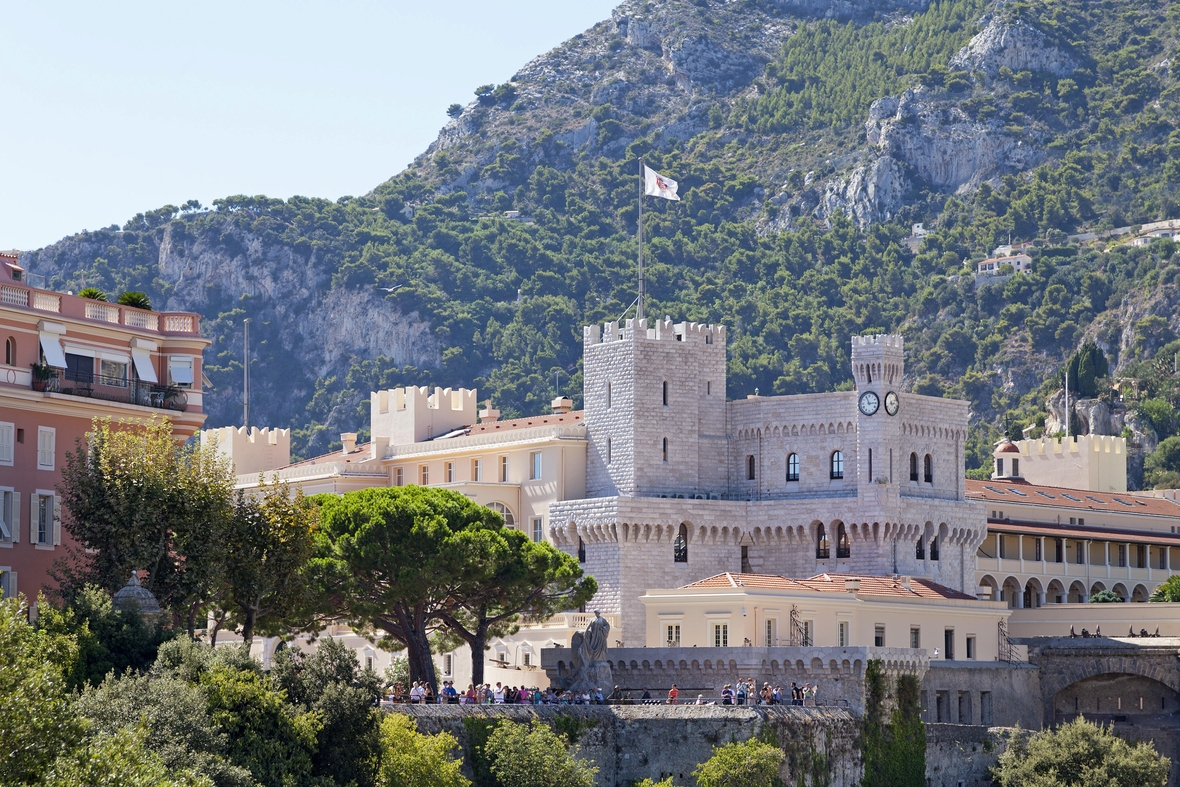 Das Bild zeigt den imposanten Fürstenpalast in Monaco, dahinter sind Berge zu sehen.
