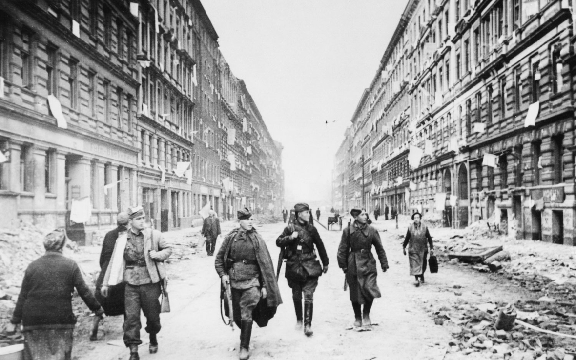 Am 1. Mai 1945 ziehen sowjetische Soldaten durch eine Straße in Berlin. Die weißen Fahnen an den Fenstern bedeuten, dass sich die Menschen ergeben.