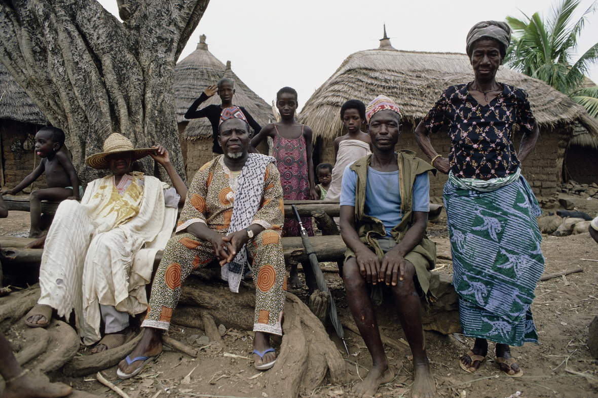 Häuptling eines Dorfes der Bassari mit seiner Familie vor den traditionellen Häusern des Volkes. 