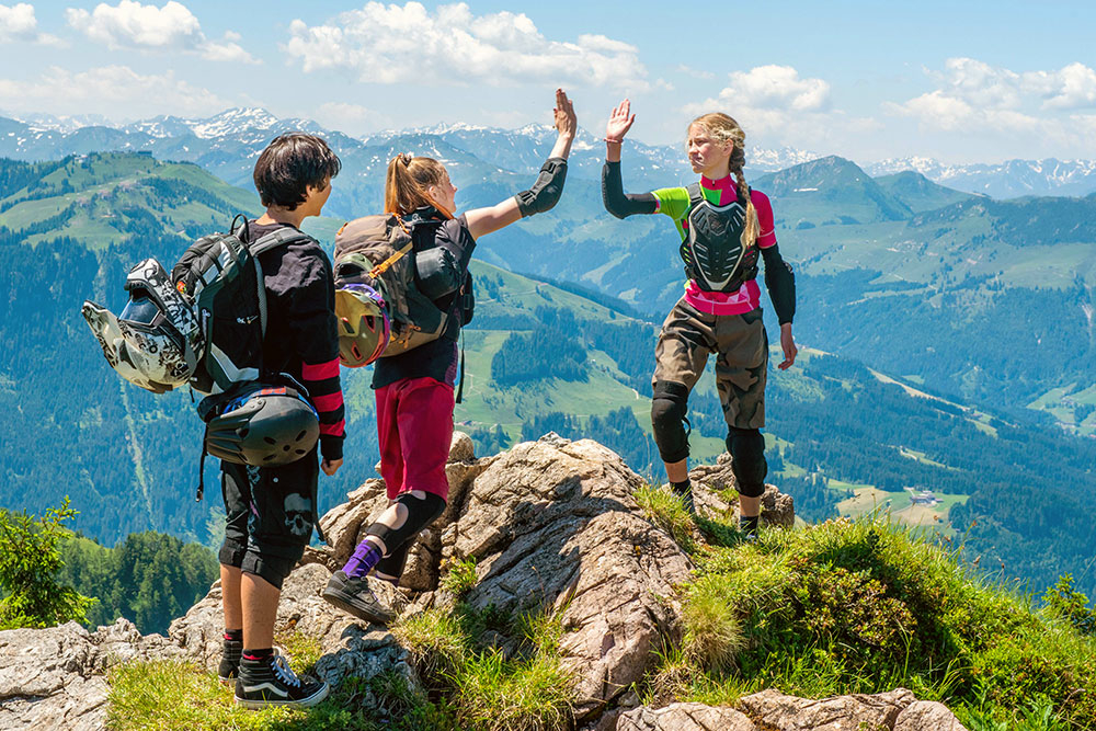 Szenenbild: Jo, Vicky und Madison (von links nach rechts) auf einem Berggipfel. Die Mädchen klatschen einander jeweils in die rechte Hand der anderen und beglückwünschen sich zum Gipfelsturm.