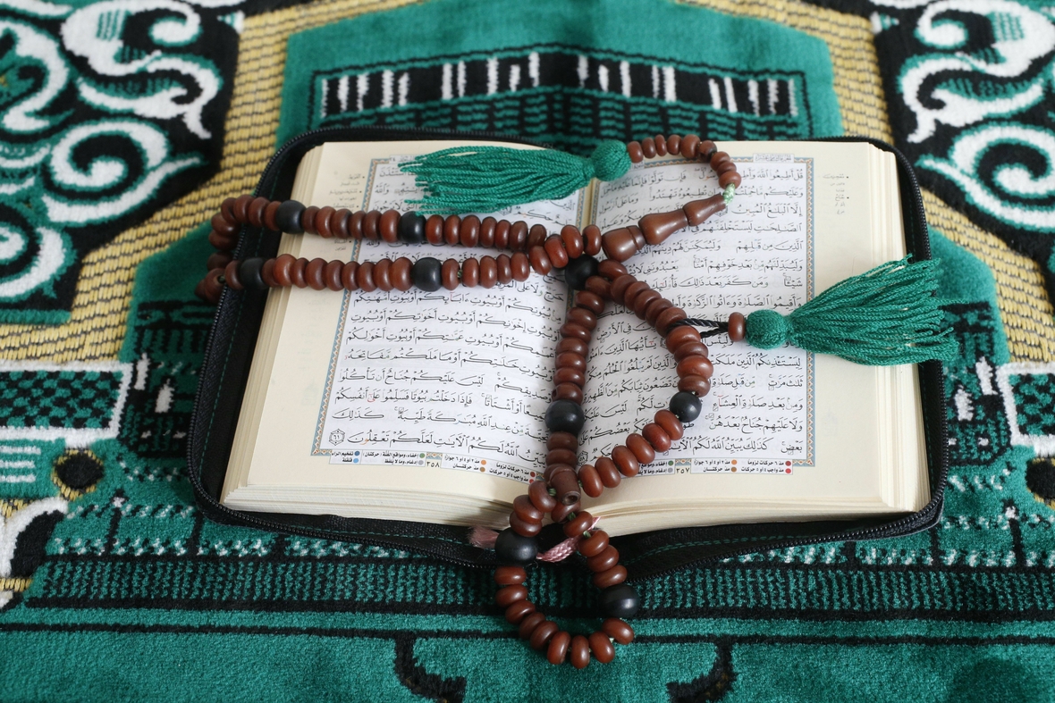 Der Koran und muslimische Gebetsperlen. Die Gebetsperlen sind auf eine Kette gefädelt und liegen auf einem geöffneten Buch.
