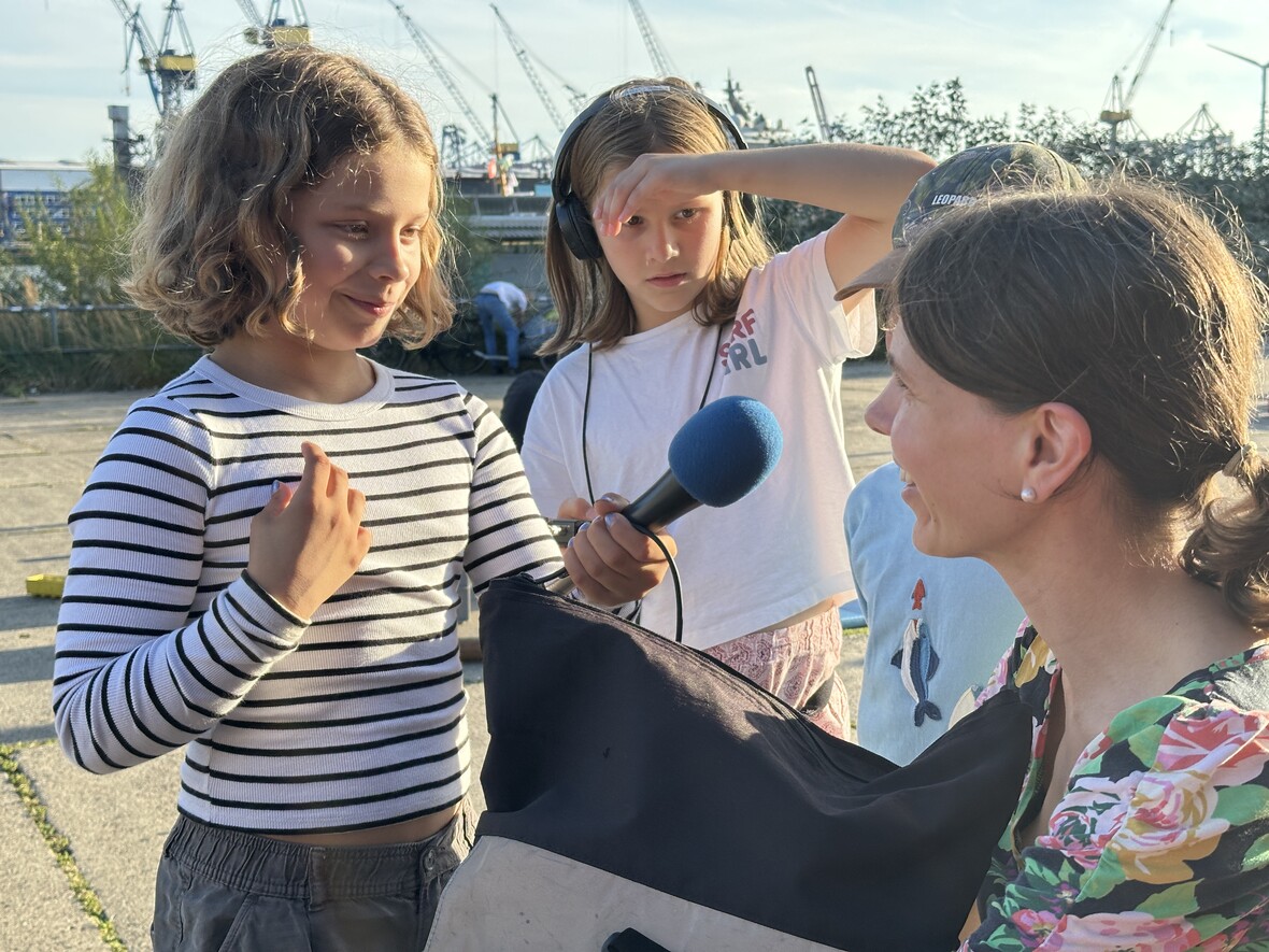 Kinder befragen sich mit einem Mikrofon draußen. 
