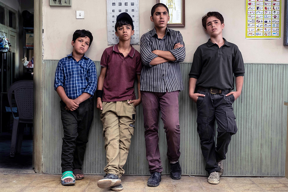 Szenenbild: Ali und seine drei engsten Freunde (von links nach rechts: Abolfazi, Reza, Mamad und Ali). Sie lehnen lässig an einer Hauswand.