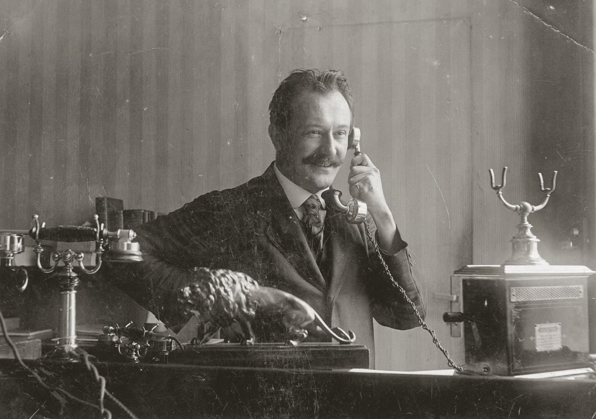 Die Schwarz-Weiß-Aufnahme zeigt einen Mann, der um 1910 telefoniert.