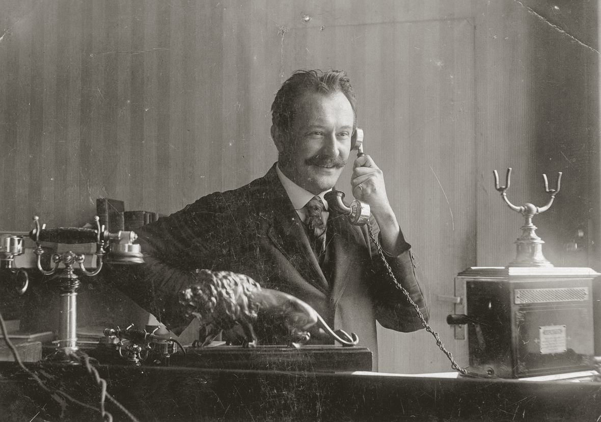 Die Schwarz-Weiß-Aufnahme zeigt einen Mann, der um 1910 telefoniert.