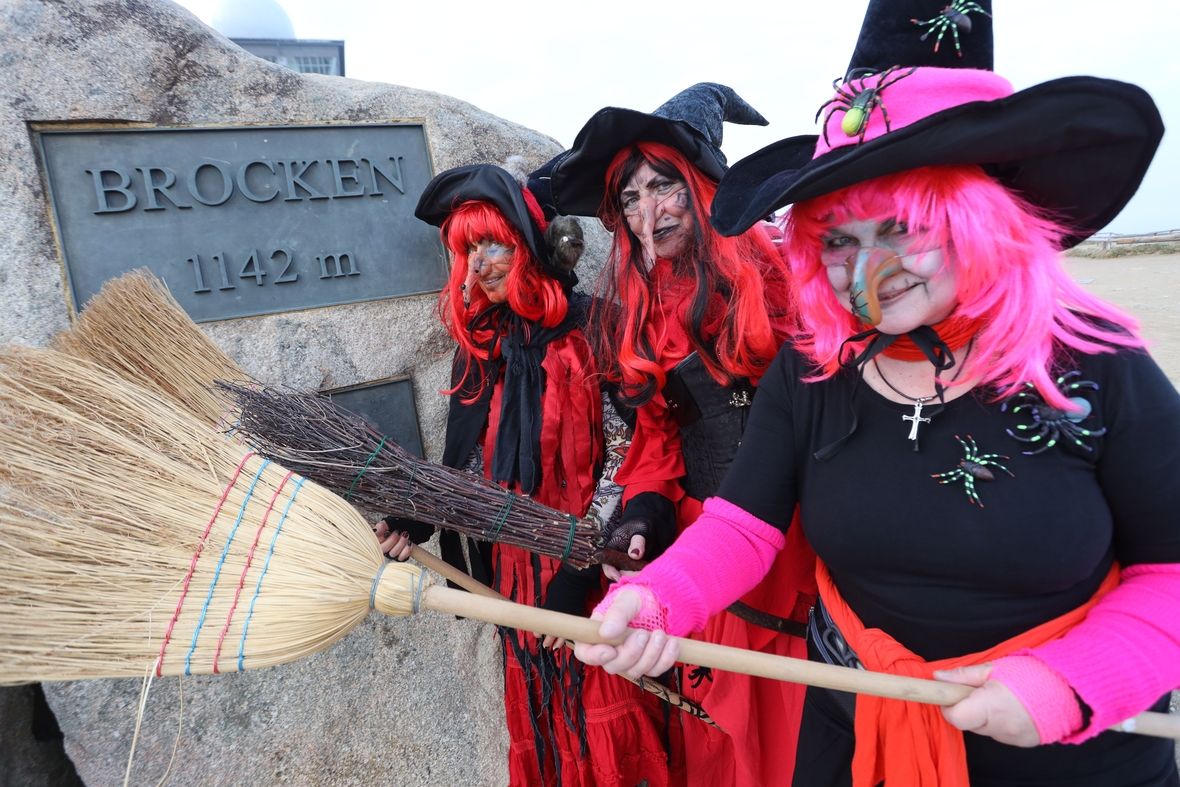 Drei als Hexen verkleidete Frauen stehen auf dem Brocken an der offiziellen Höhenmarke. Sie feiern die Walpurgisnacht.