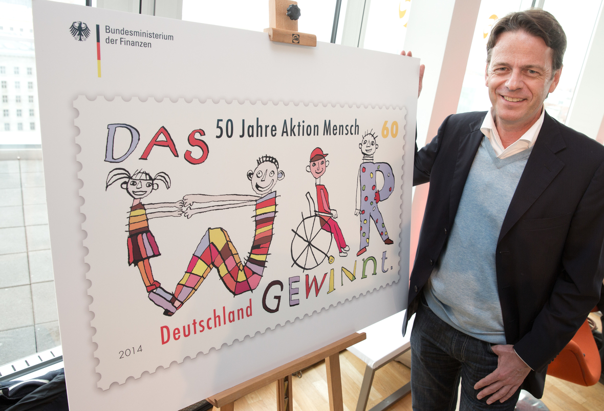 2014: Moderator Rudi Cerne neben einer zum 50. Jubiläum herausgegebenen überdimensionalen "Aktion Mensch"-Sonderbriefmarke 