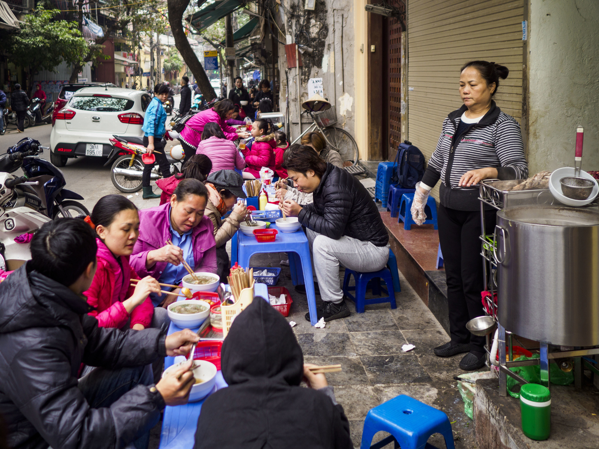 Eine Frau beobachtet ihre Kunden an ihrem "Pho" -Stand in der Altstadt von Hanoi. Pho ist eine vietnamesische Rindfleischnudelsuppe und wird zu jeder Tageszeit gegessen. Die Altstadt ist das Herz von Hanoi, mit engen Gassen und vielen kleinen Läden.