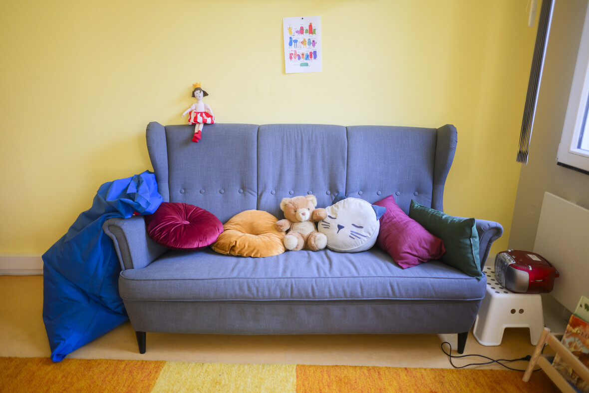 Blaues Sofa dekoriert mit Kuscheltieren und Kissen in einem Raum mit gelben Wänden. 