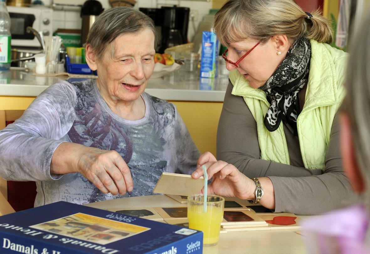 Bewohnerin eines Altenpflegeheim und eine Betreuerin spielen "Damals & Heute" mit Karten