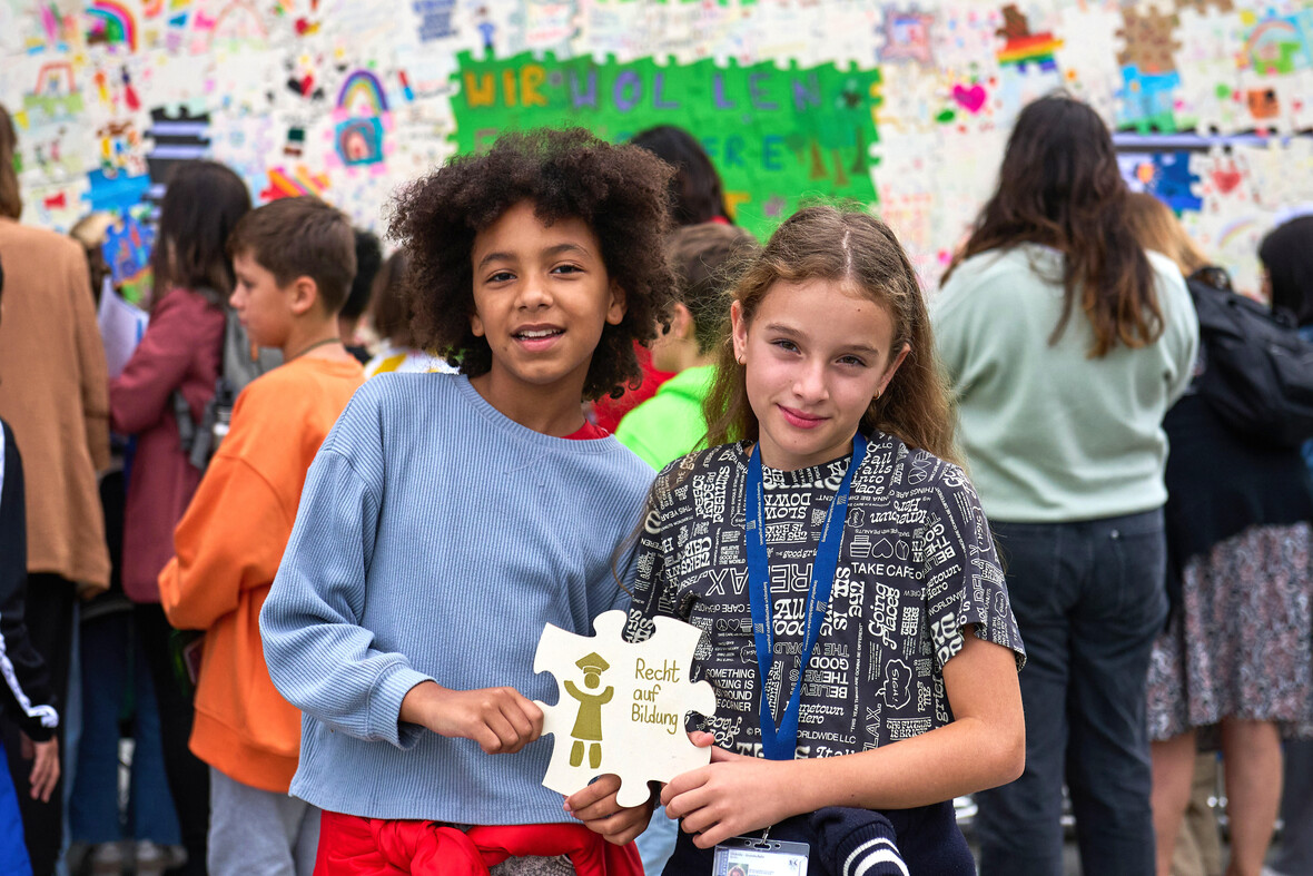 Zwei Kinder halten ein großes Puzzleteil mit der Aufschrift ‚Recht auf Bildung‘.