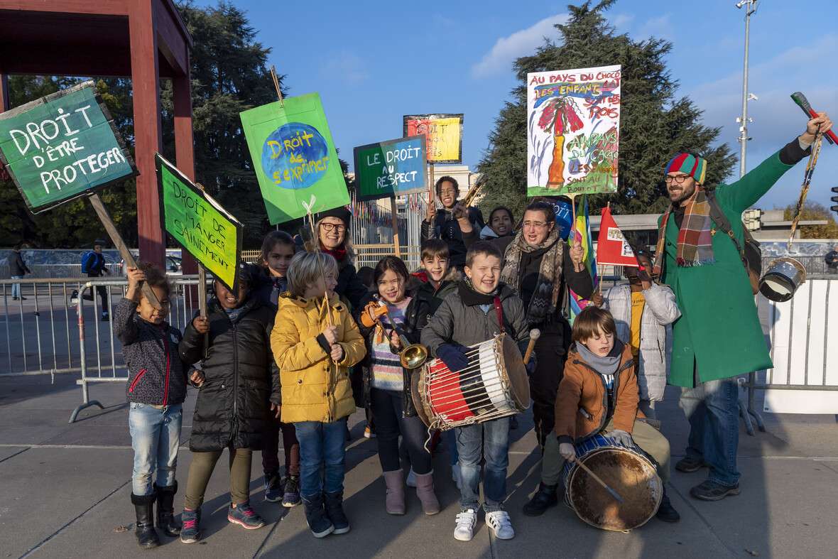Gruppe von Kindern und Erwachsenen demonstriert mit bunten Schildern und Trommeln für Kinderrechte.